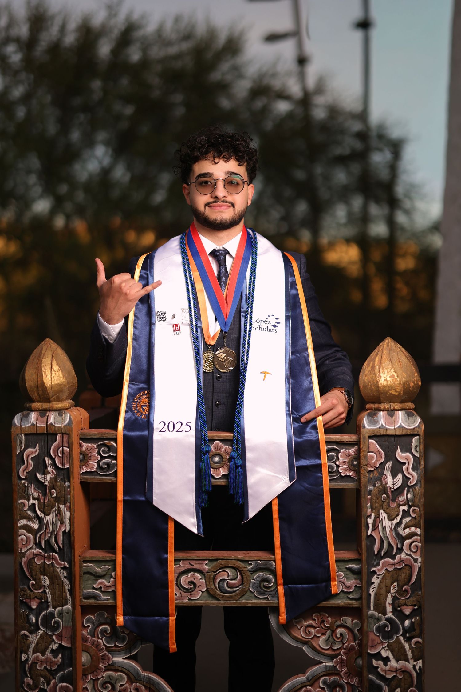A graduate in a blue and white stole poses for a series of celebratory photos outdoors at sunset.