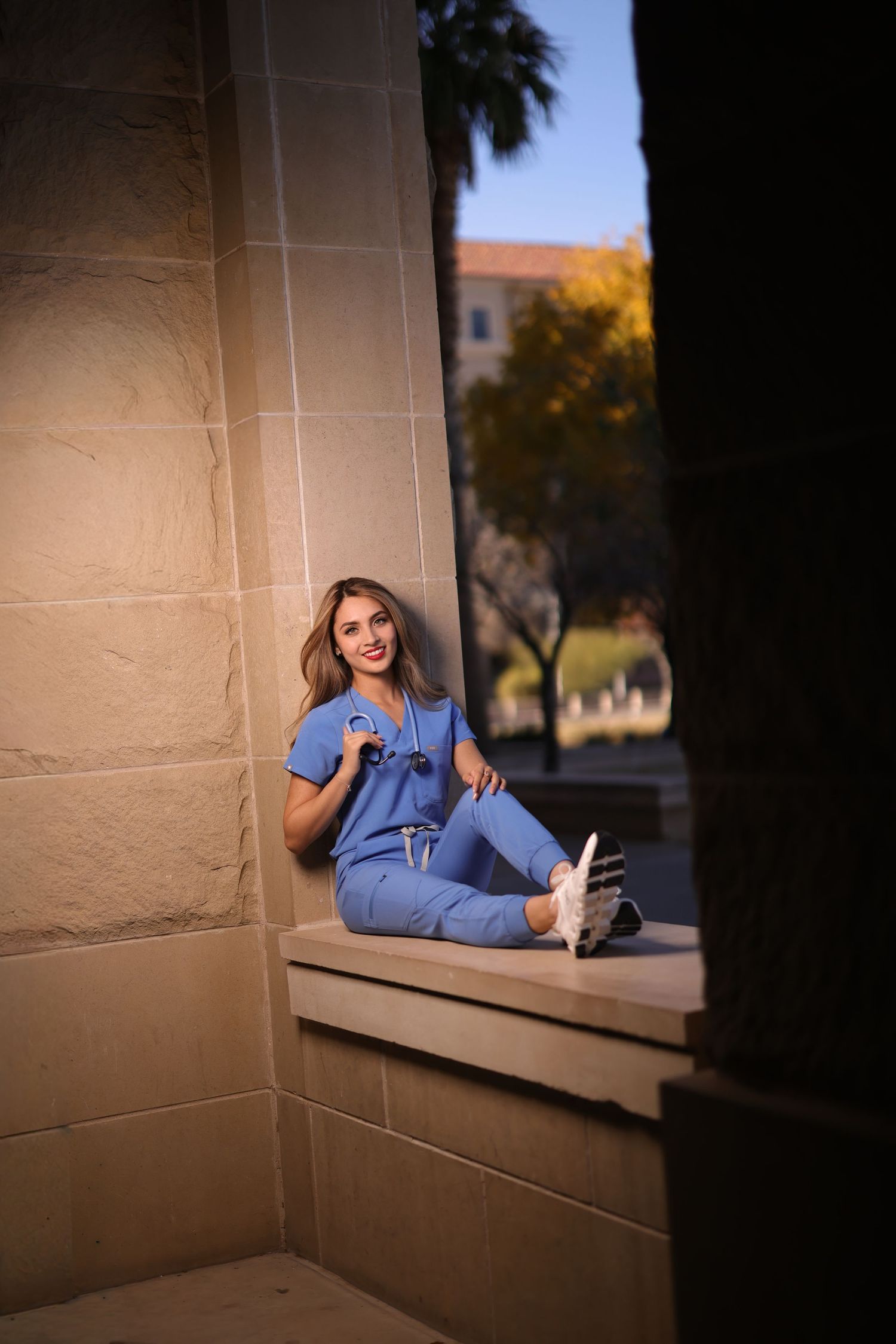 A person in blue scrubs lounges on a window ledge in a medical building during golden hour lighting.