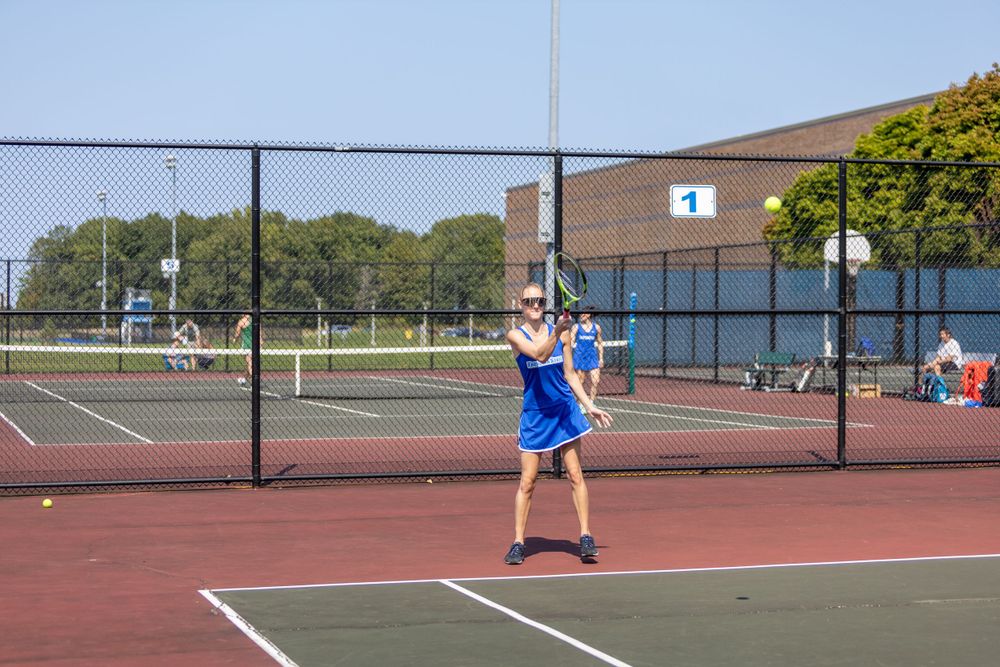 Tennis player practicing serves on an outdoor court during training.