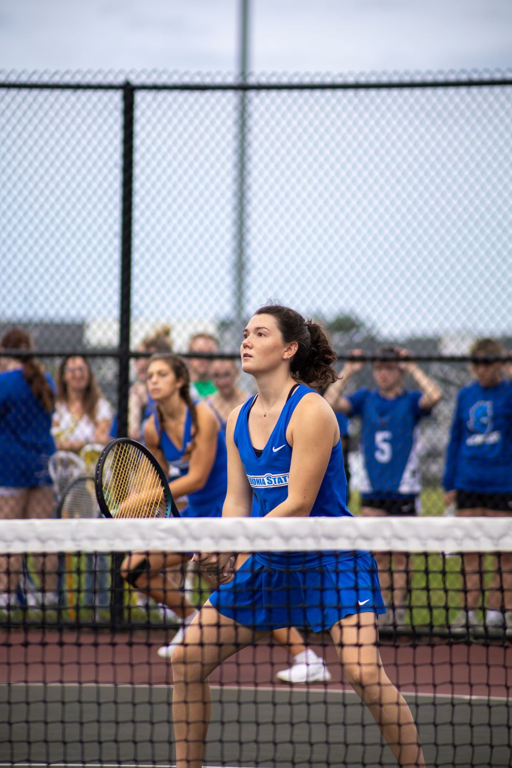 Tennis players in blue uniforms positioned at net during competitive match.