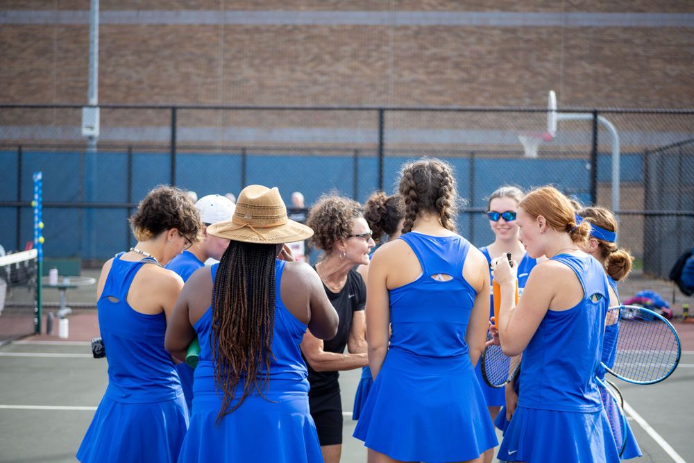 Team of tennis players in blue uniforms gathered together on court.