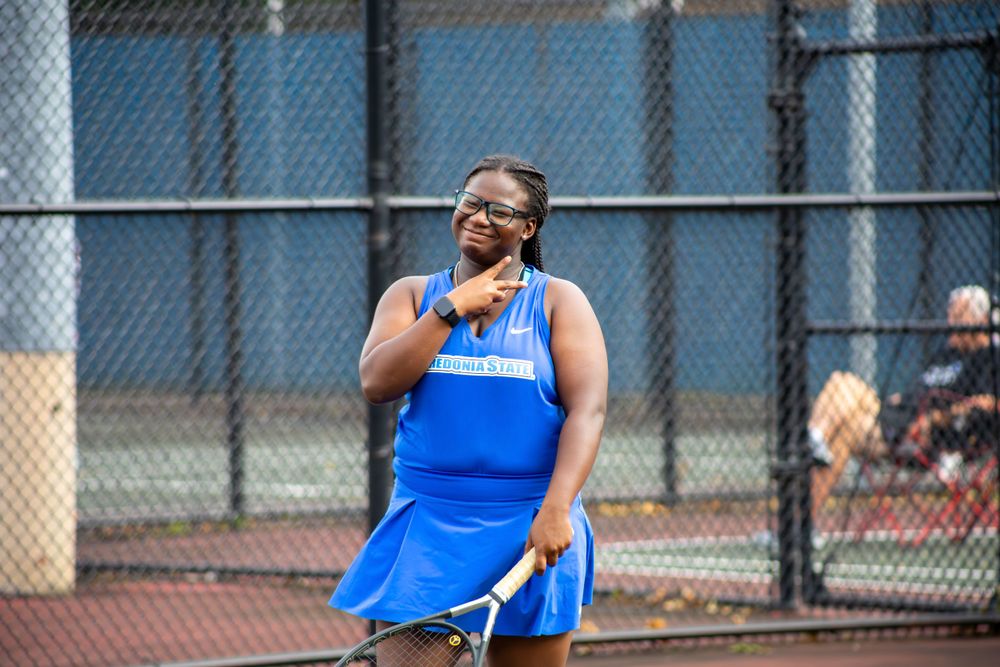 Tennis player in blue uniform serves ball during outdoor match.