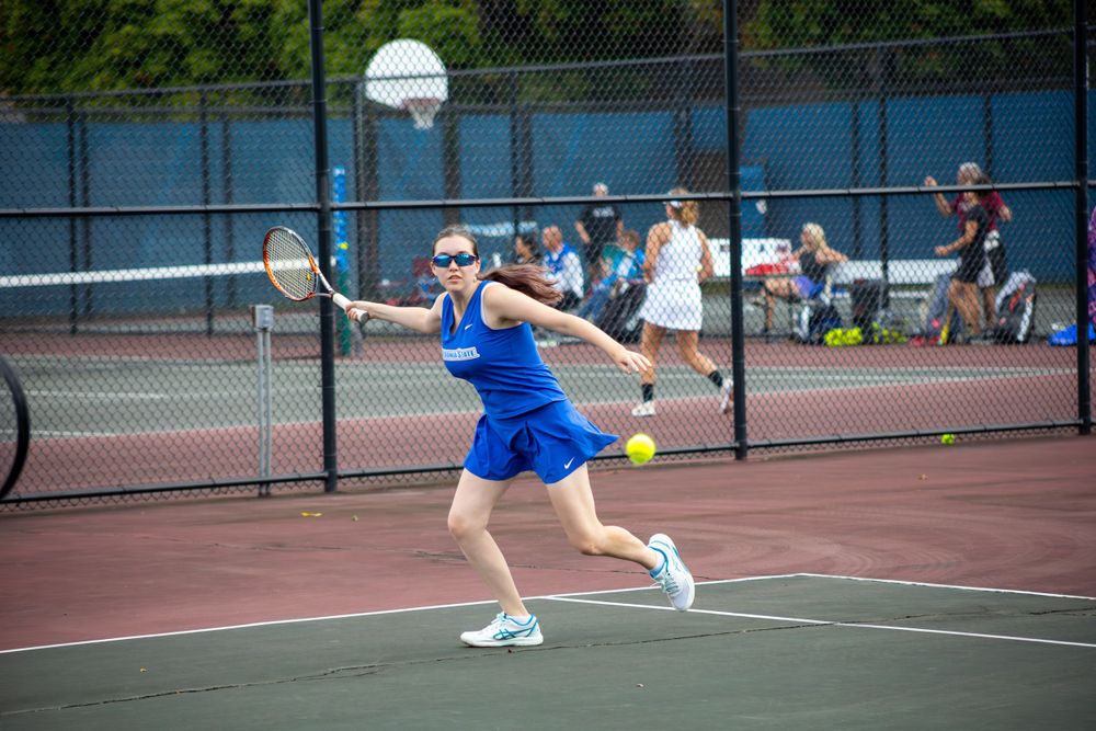 Tennis player stretches to make a forehand return on outdoor court.
