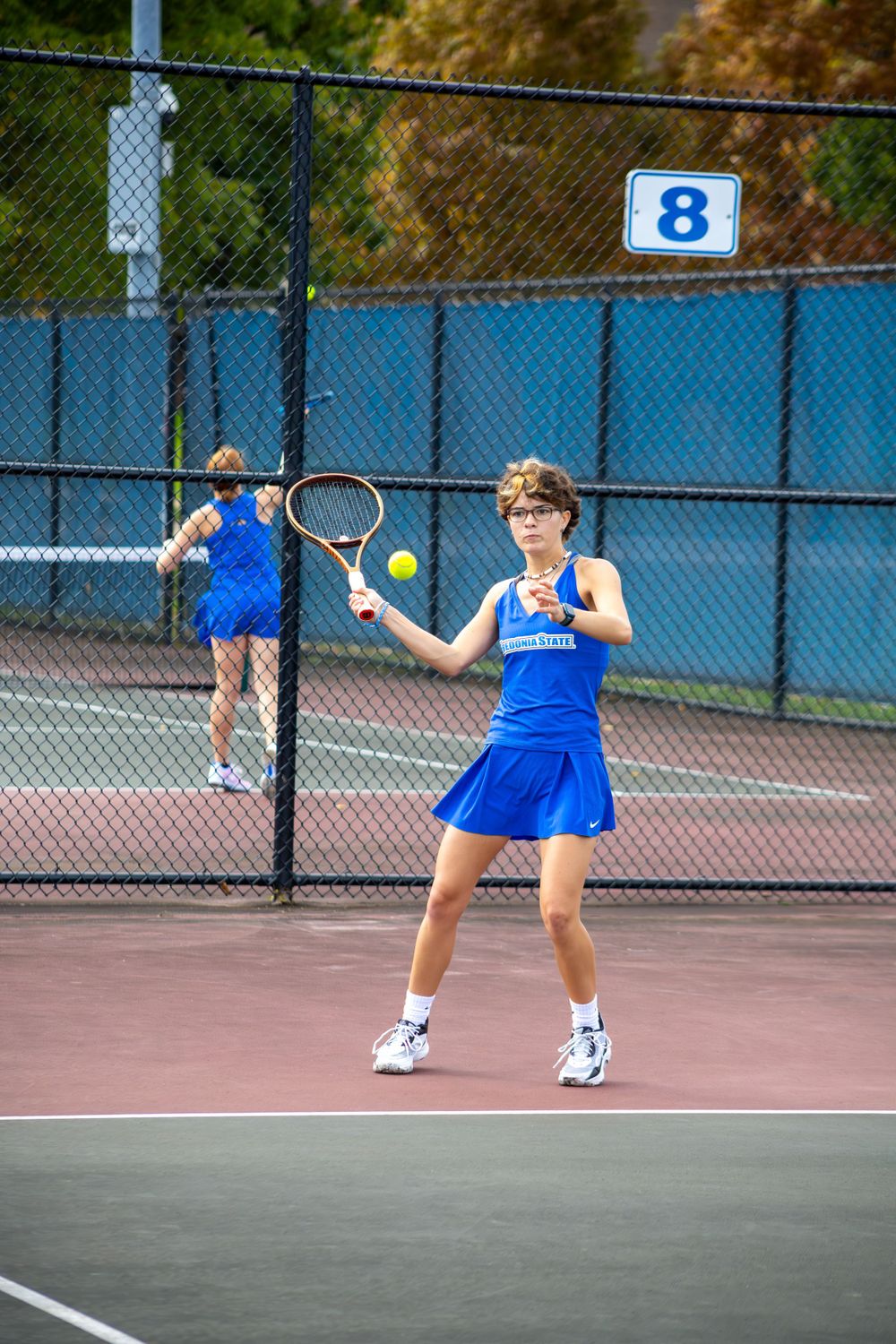 Tennis players in blue uniforms practice serves and returns on outdoor courts.