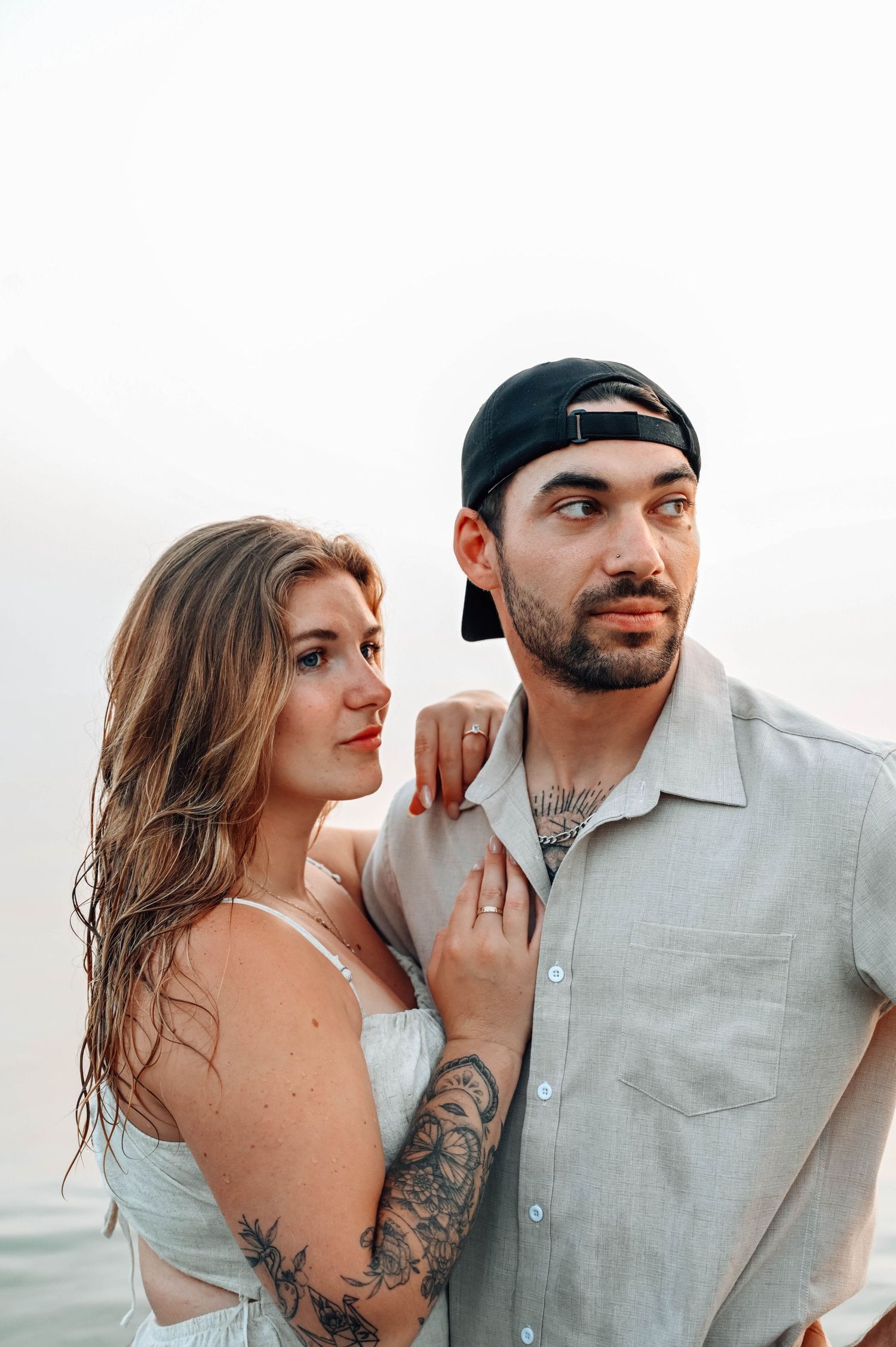 Couple in casual attire posing against minimal white background.
