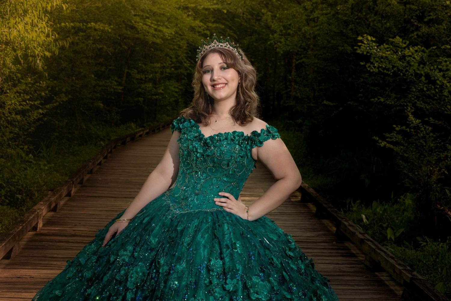 Elegant emerald gown with off-shoulder design on wooden bridge pathway.