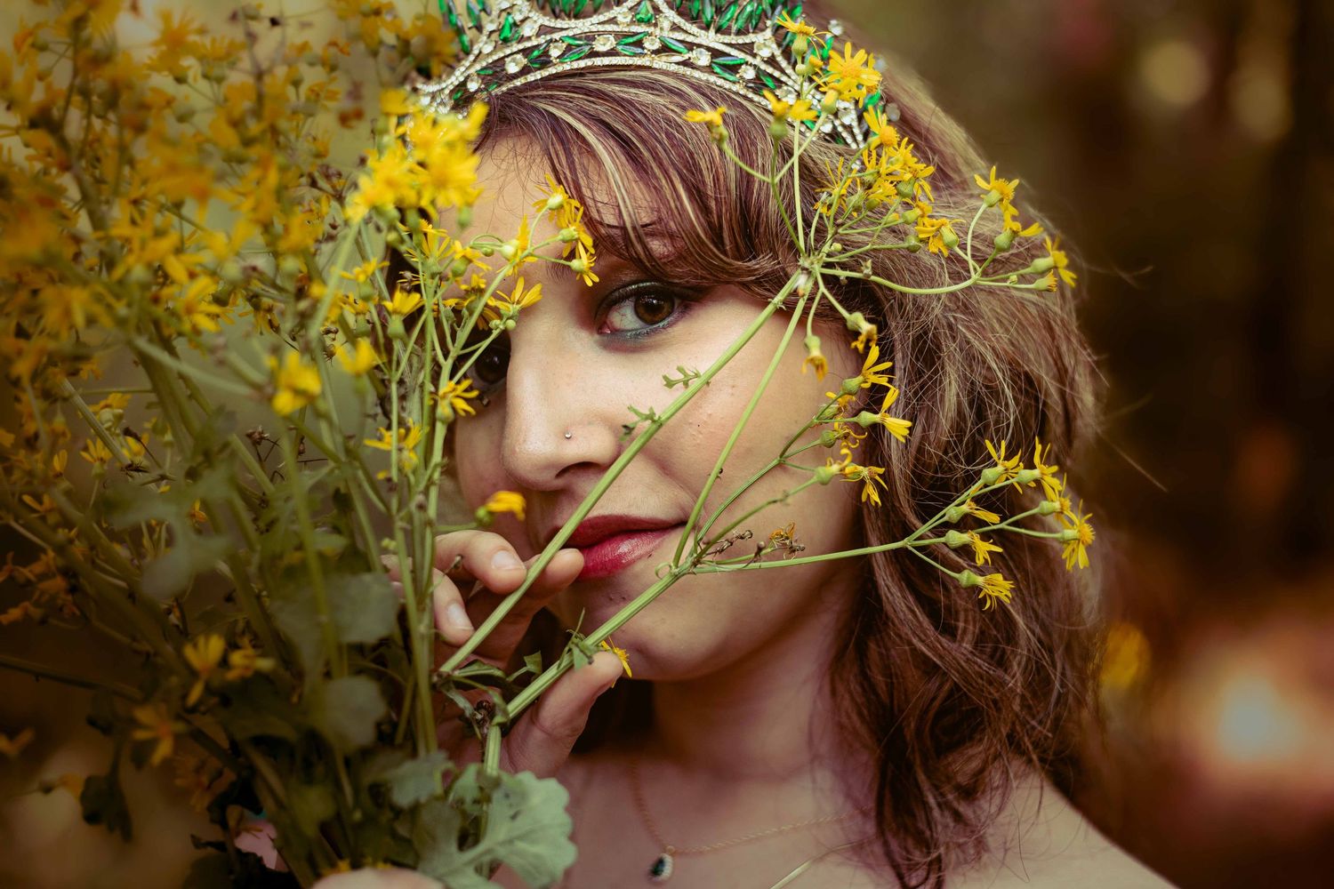 Artistic portrait in a forest setting with yellow wildflowers and emerald green gown details.