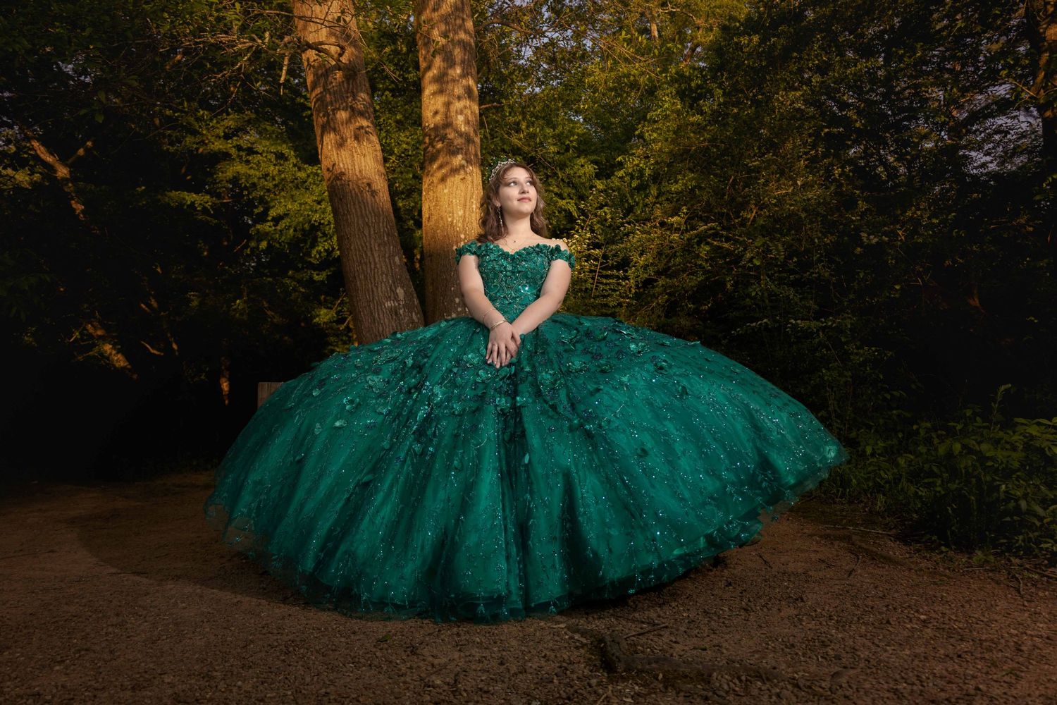 Elegant emerald ball gown photographed against tall trees in a woodland setting.