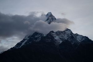 Dramatic snow-covered mountain peaks rise against a moody cloudy sky in a panoramic view.
