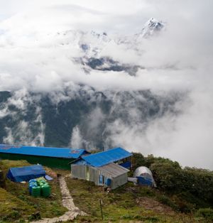 Blue-roofed mountain lodges perched on a green hillside with misty peaks in the background.