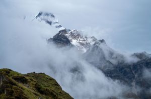 Cloudy mountain peaks shrouded in mist against a light blue sky.