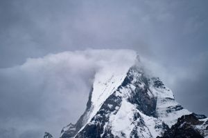 Dramatic snow-covered mountain peaks emerge through dark stormy clouds.