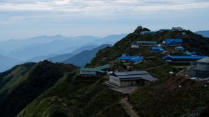 Mountain lodges with blue roofs perched on a ridgeline overlooking misty mountain ranges in the distance.