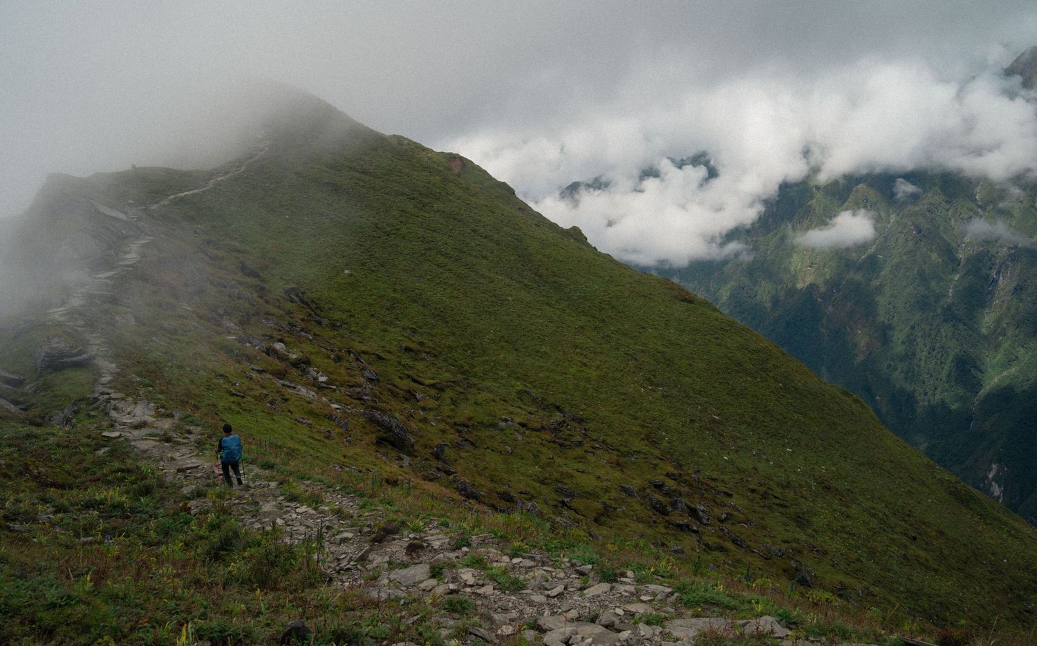 Rugged mountain landscape with green slopes and misty peaks under cloudy skies.