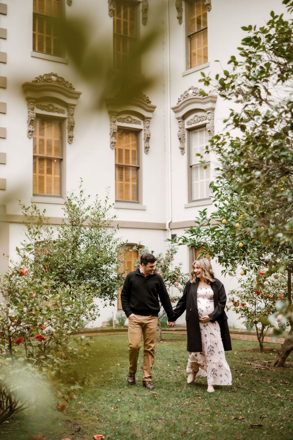 Couple poses together in front of a historic building with rose bushes in the garden.