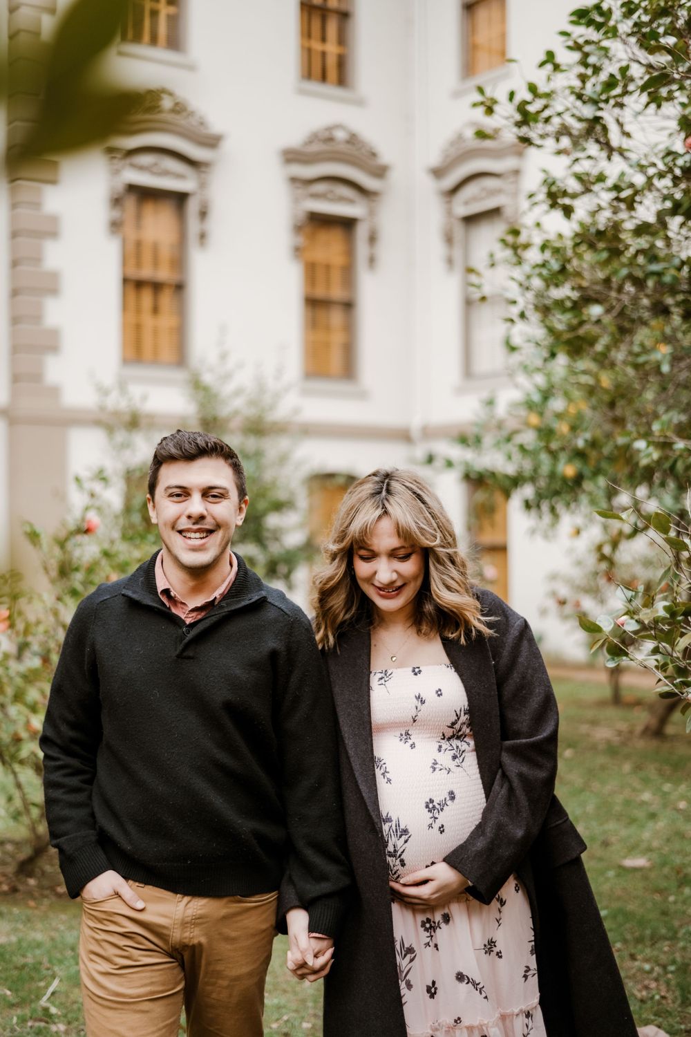 Couple sharing a romantic moment in front of an elegant building with rose gardens.