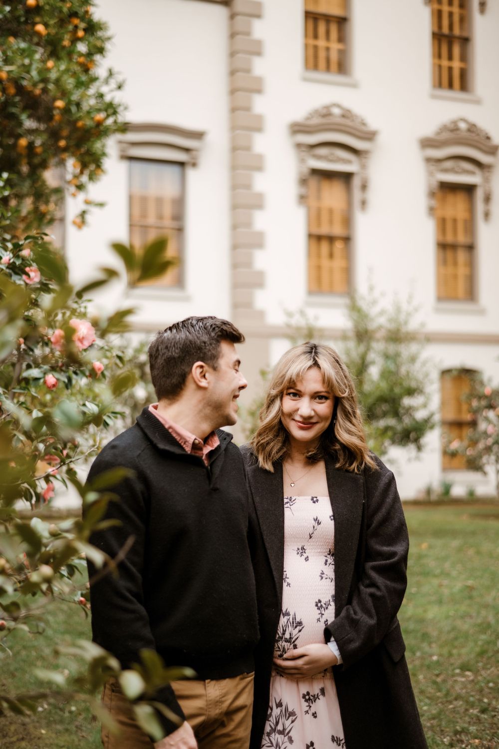 Couple laughing together in front of a historic building surrounded by blooming rose bushes.