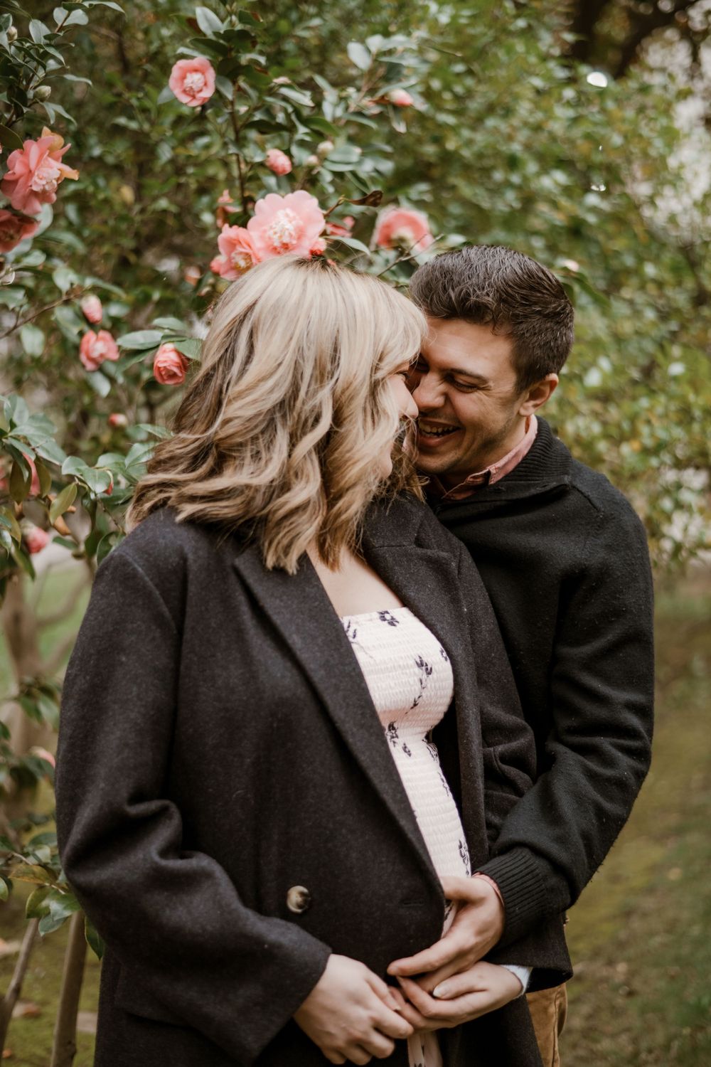 A romantic maternity photoshoot in a garden with pink roses as a couple shares an intimate moment.