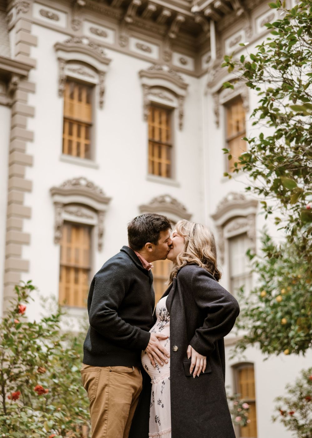 A romantic couple embraces in front of a historic building with ornate architecture.