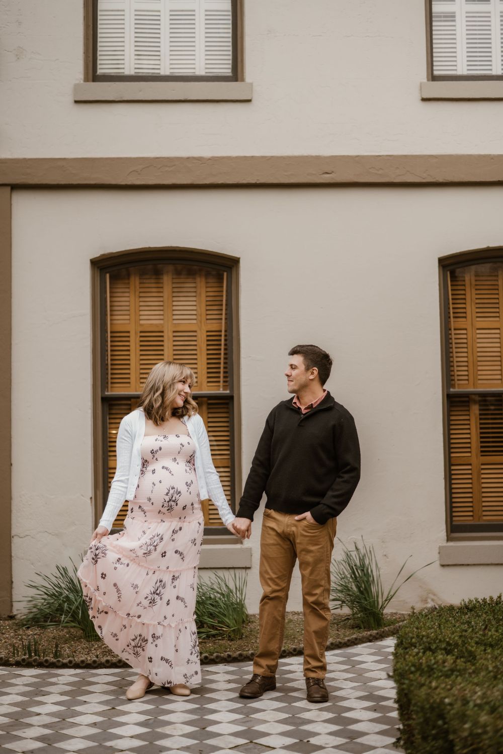 A couple shares a playful moment on a patterned walkway beside a classic building.