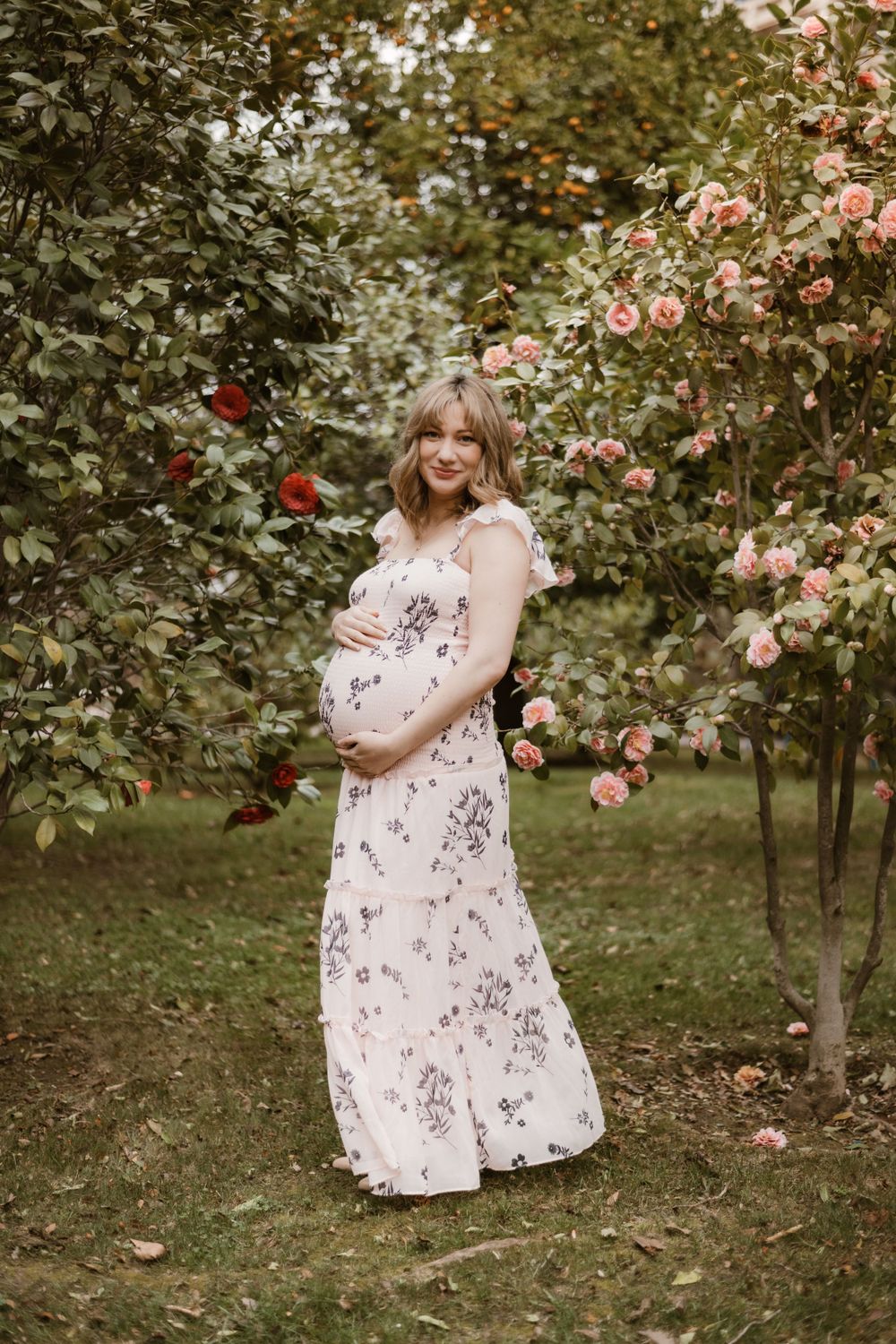 A maternity portrait in a rose garden featuring a floral maxi dress.