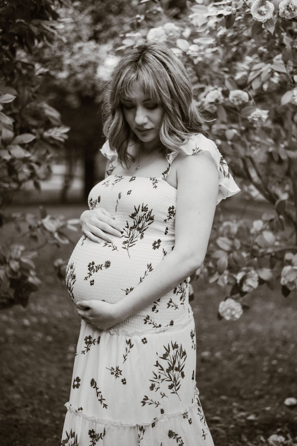 A black and white maternity portrait showcasing an expectant moment in a garden setting.