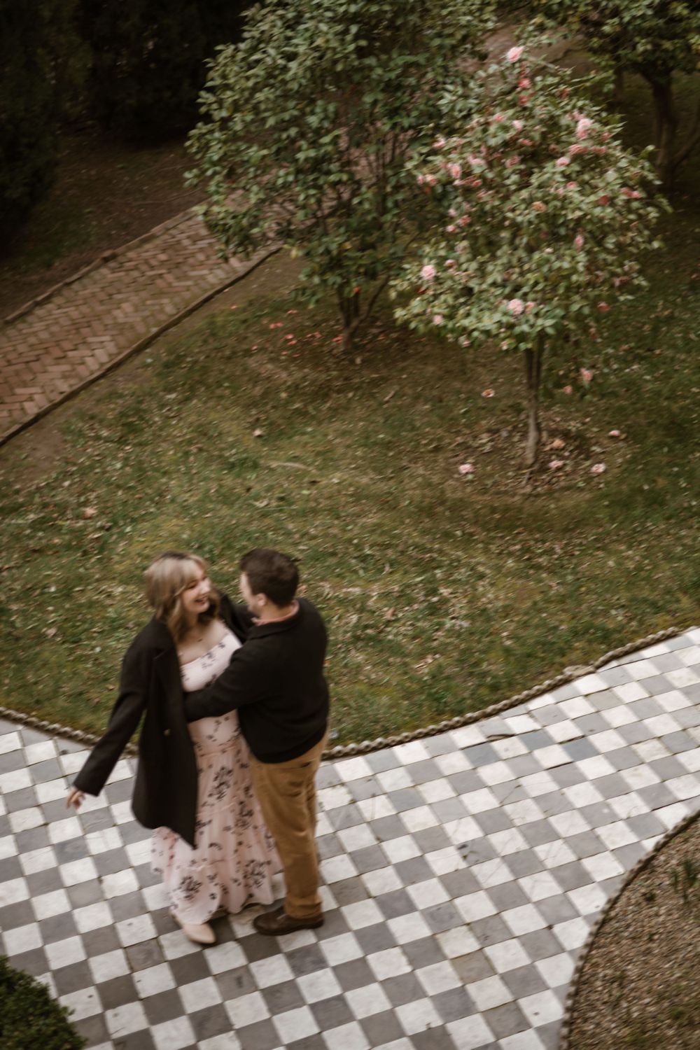 An aerial view of a couple standing on a checkered pathway surrounded by garden trees.