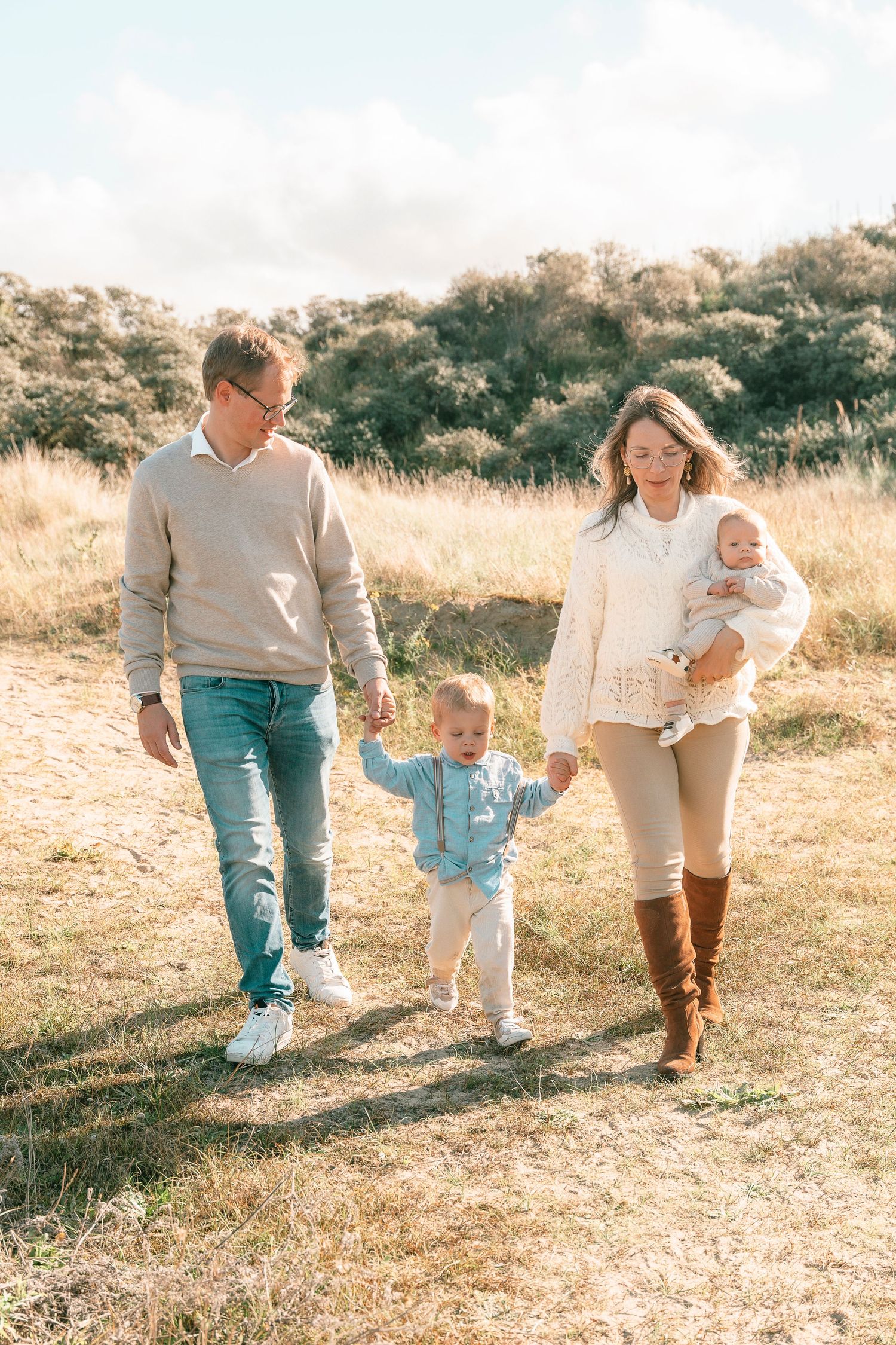 A casual family stroll through a sun-drenched autumn field with rolling hills in the background.