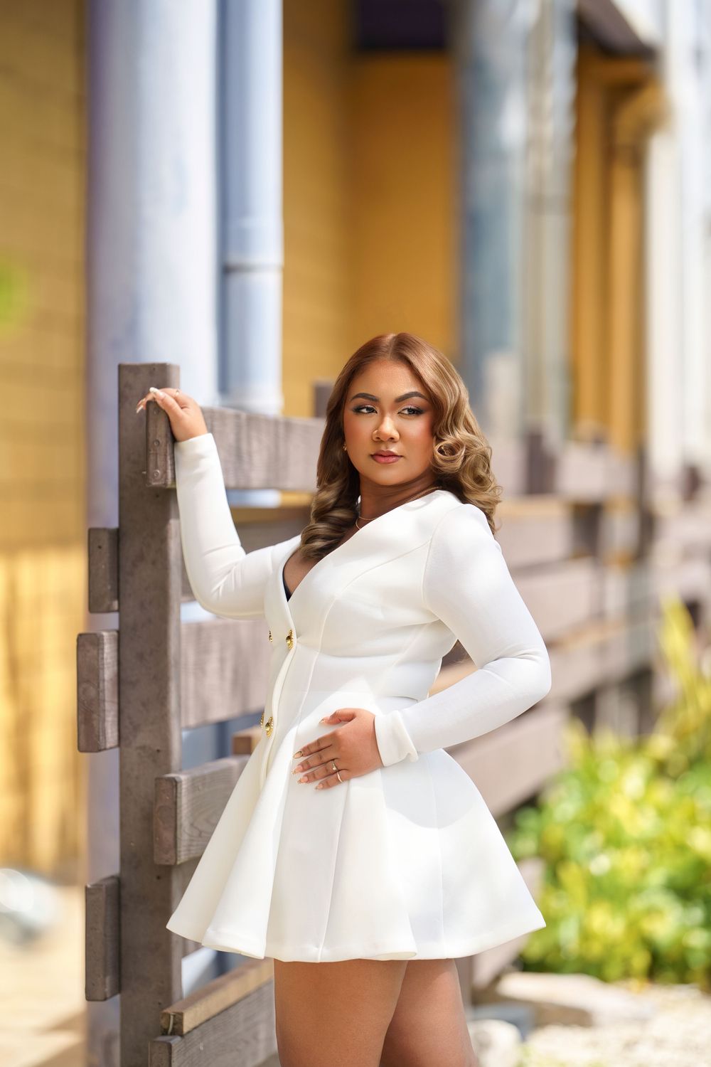 A person in a stylish white long-sleeved mini dress poses elegantly against an outdoor railing.
