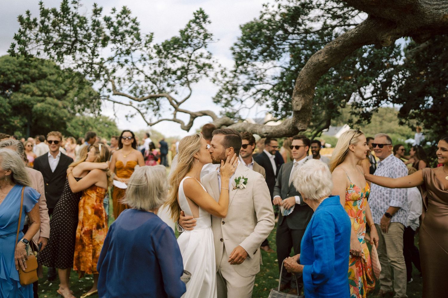 Couple in light wedding attire embraces on sandy dunes with mountain backdrop.