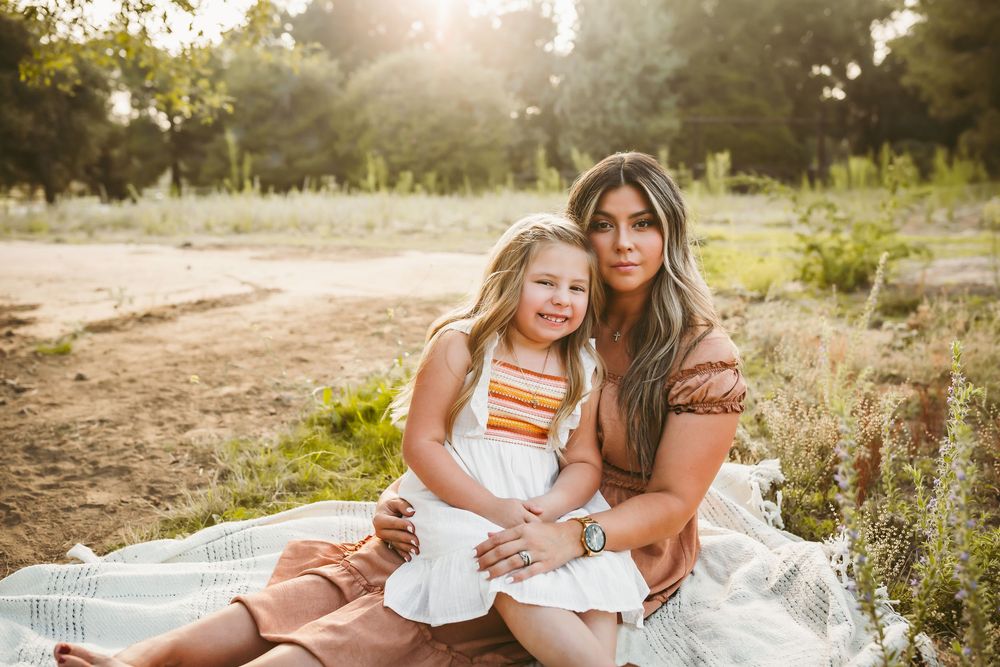 A tender outdoor portrait of two people sitting on a white blanket in golden sunlight during sunset.