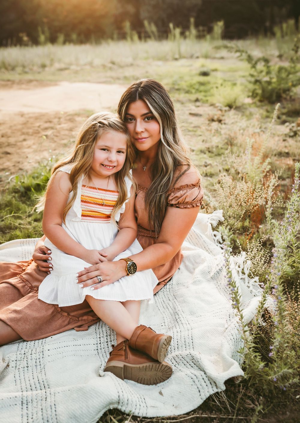 A tender outdoor photoshoot in a field at golden hour with matching white dresses and natural lighting.