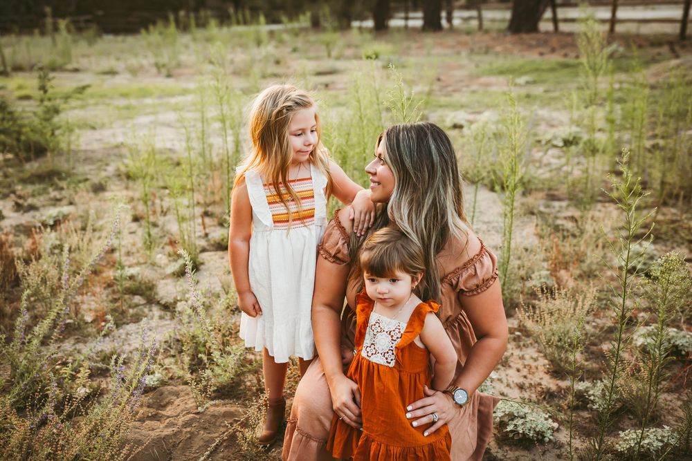 A family in burnt orange and white outfits shares tender moments together in a grassy outdoor setting during sunset.