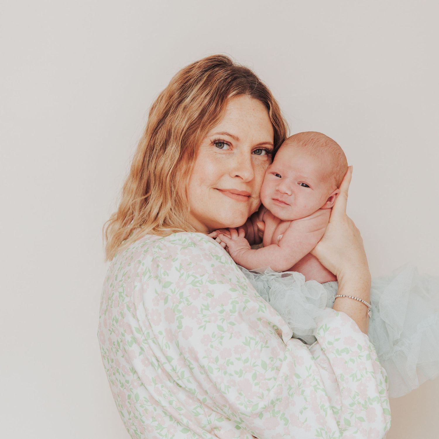 Mother holding her newborn baby close in a soft, natural light portrait.