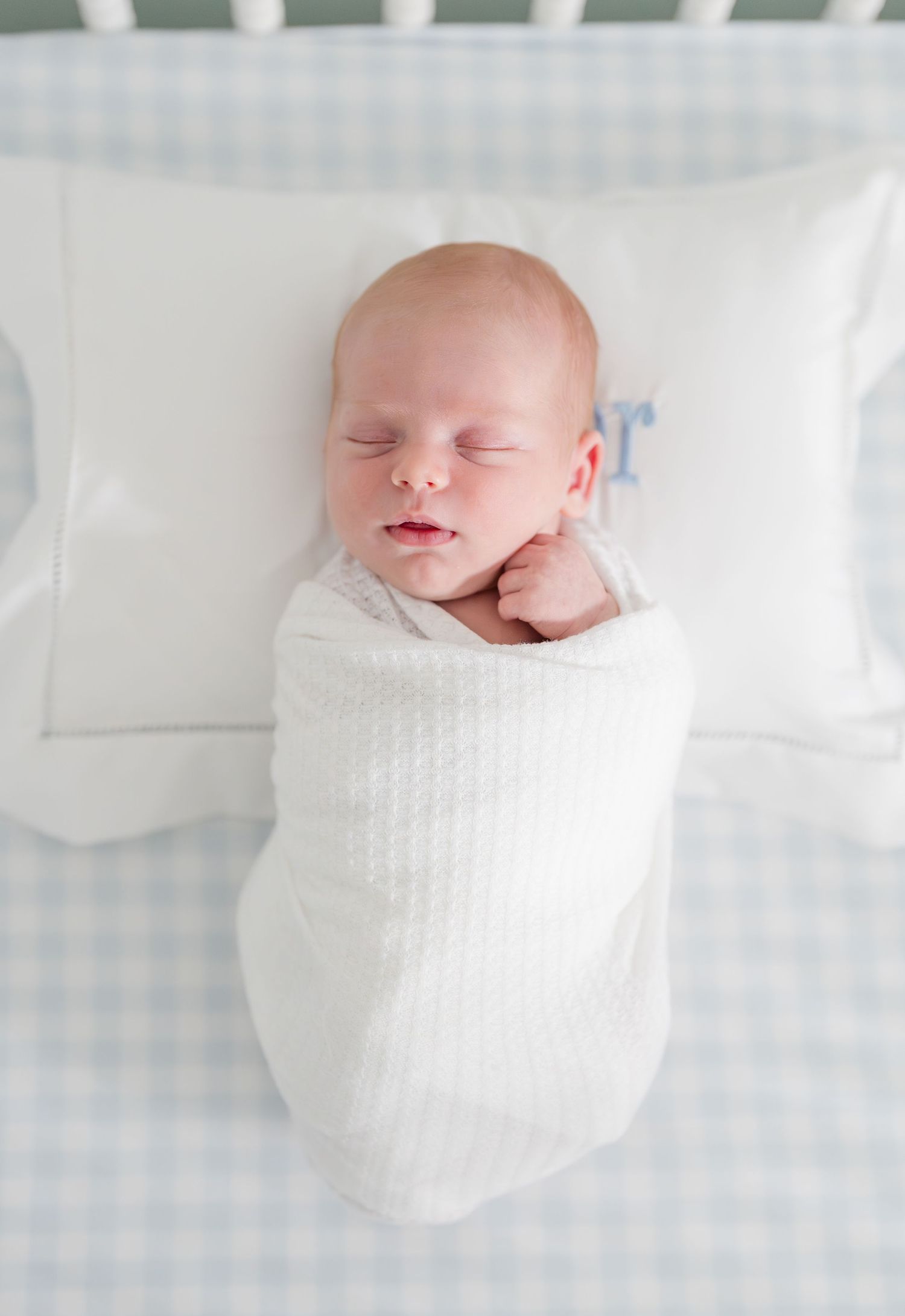 A sleeping newborn baby wrapped in a white knit blanket on crisp white bedding.