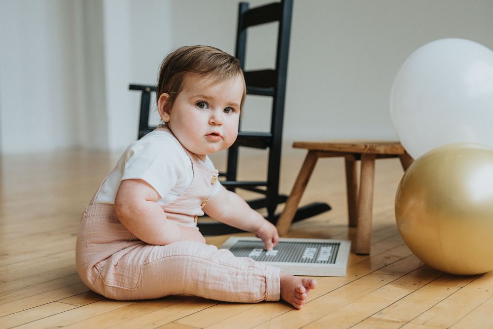 Small child in pink outfit sits on hardwood floor with digital tablet and exercise ball nearby.