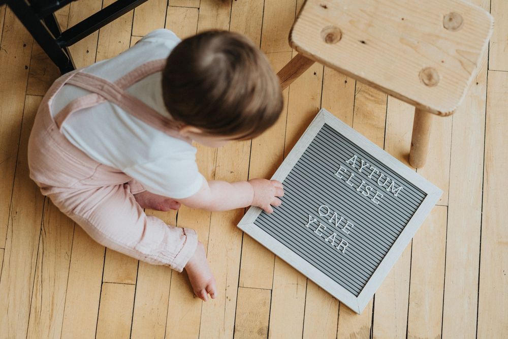 Gray letter board and baby lying on light wooden floor with playful expression.