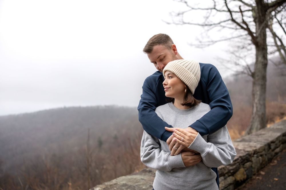 A couple embraces in a romantic winter engagement photoshoot against a misty mountain backdrop.