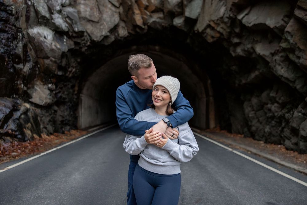 A couple in blue and white outfits embrace and laugh together during an outdoor photo session.