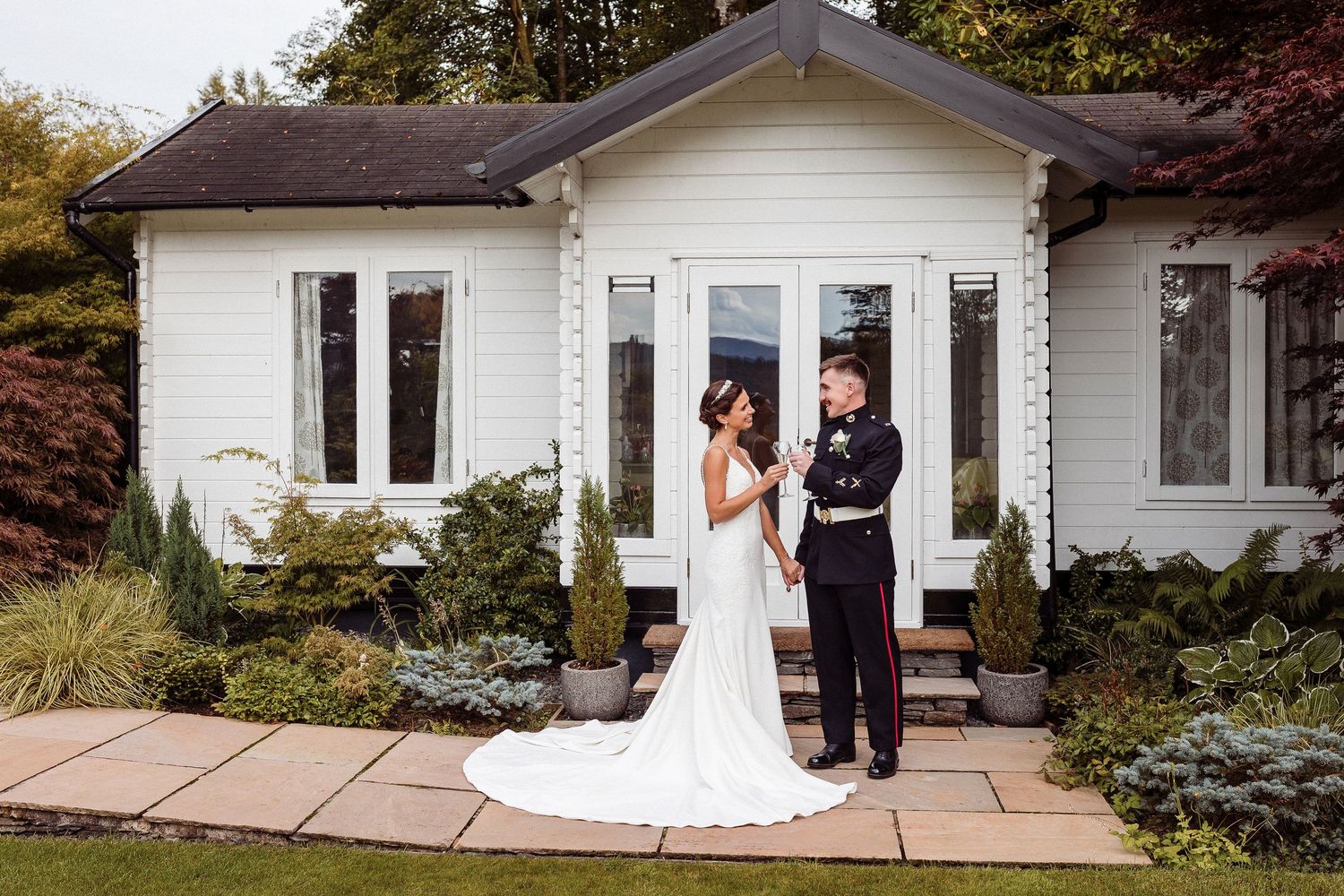 A couple shares a tender moment on a patio outside a white ranch-style house during a wedding photoshoot.