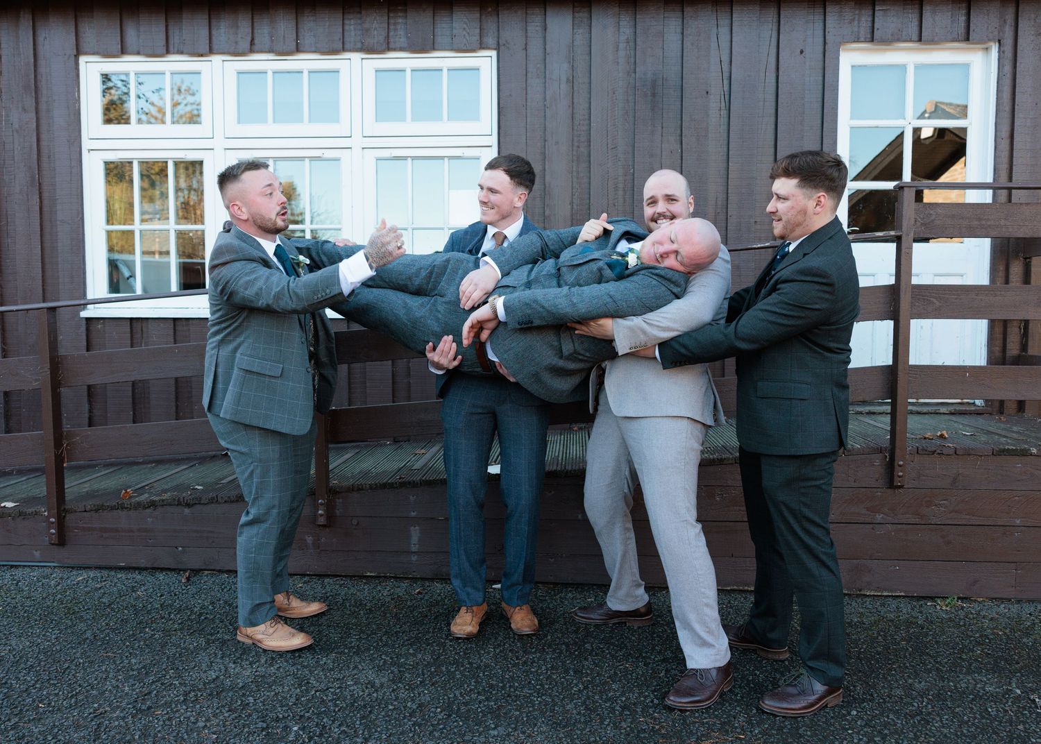 A sequence of four photos showing groomsmen playfully pushing each other in a line outside a rustic wooden building.