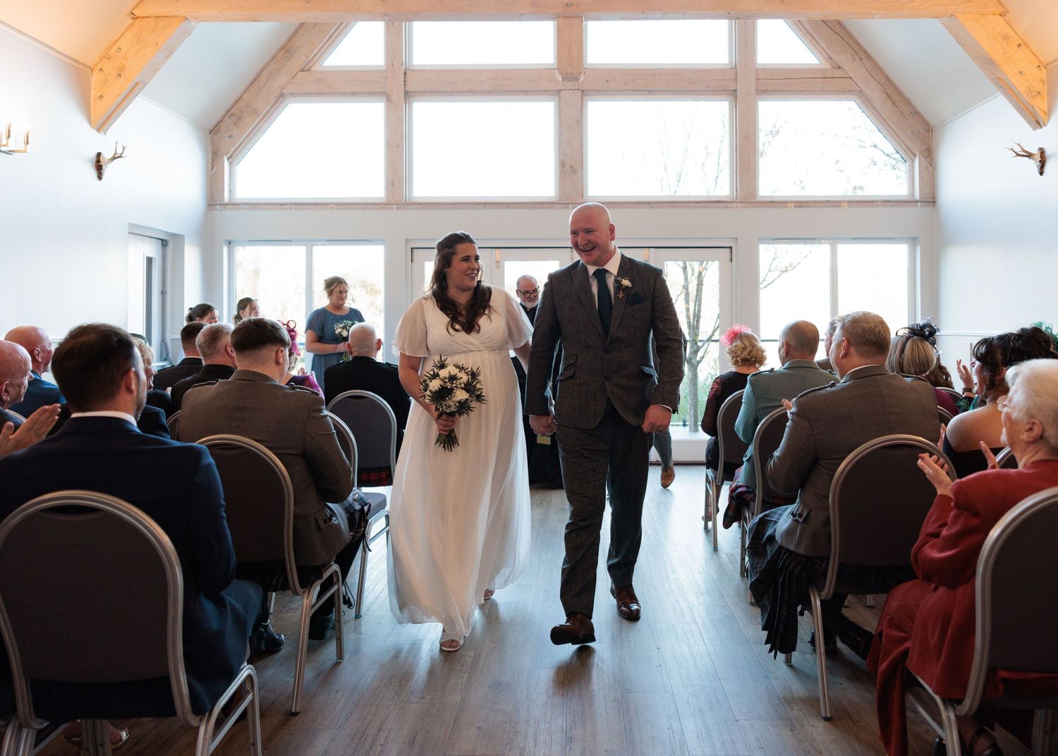 A wedding ceremony panorama shows guests seated in rows as a couple exchanges vows at the altar.