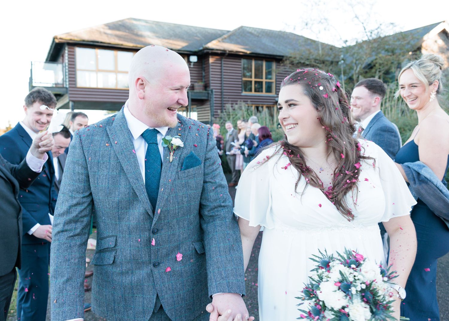 A joyful wedding couple shares a moment together outdoors with guests in the background on their special day.