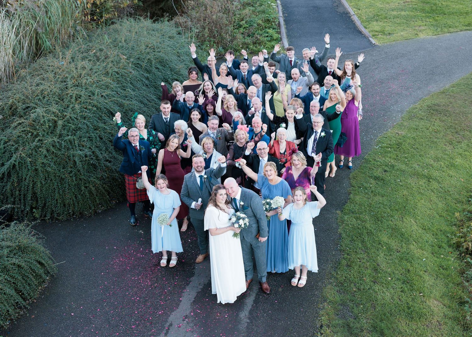 Aerial view of wedding guests gathered on a curved pathway surrounded by ornamental grasses.