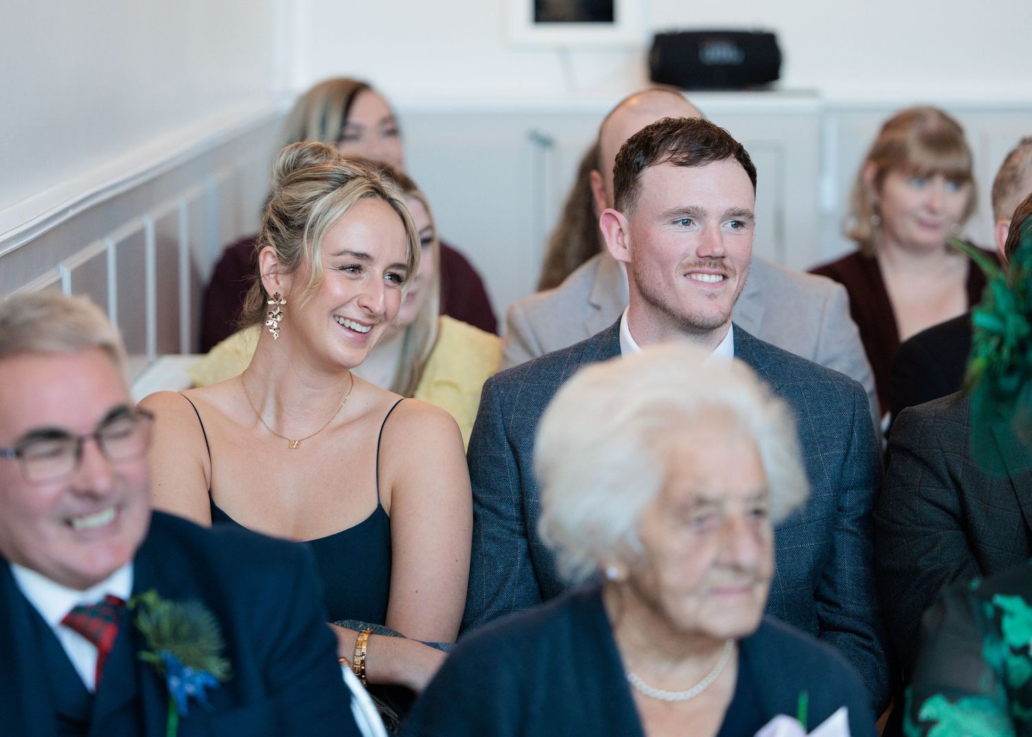 People gathered at a formal event, with some wearing evening attire and others in formal suits, sharing joyful expressions.