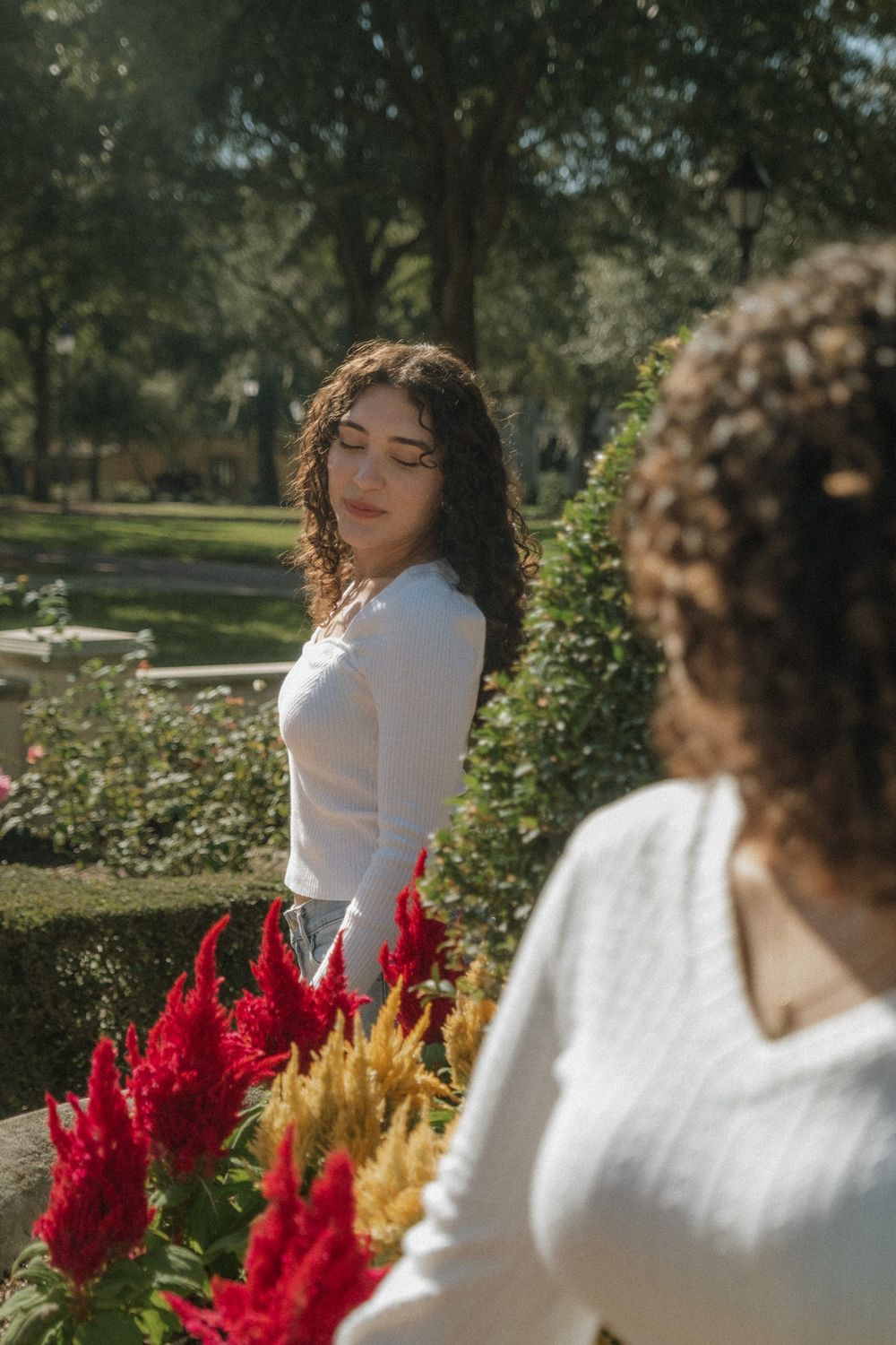 Two people posing by vibrant red celosia flowers in a garden setting.