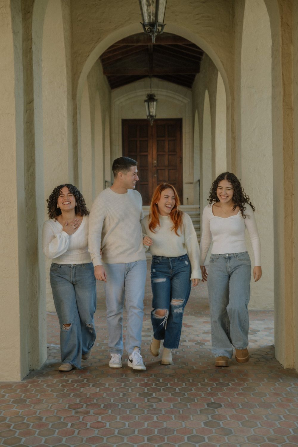 A group of friends walking together in matching white tops and jeans through an arched hallway.