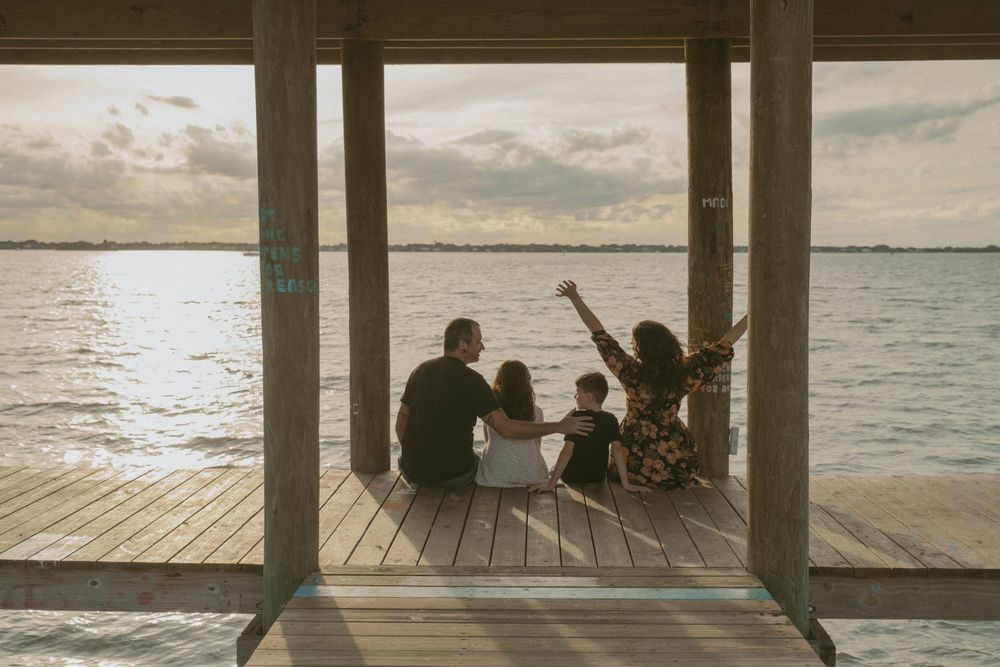 Silhouettes of people gathered under a pier structure at sunset near the ocean.