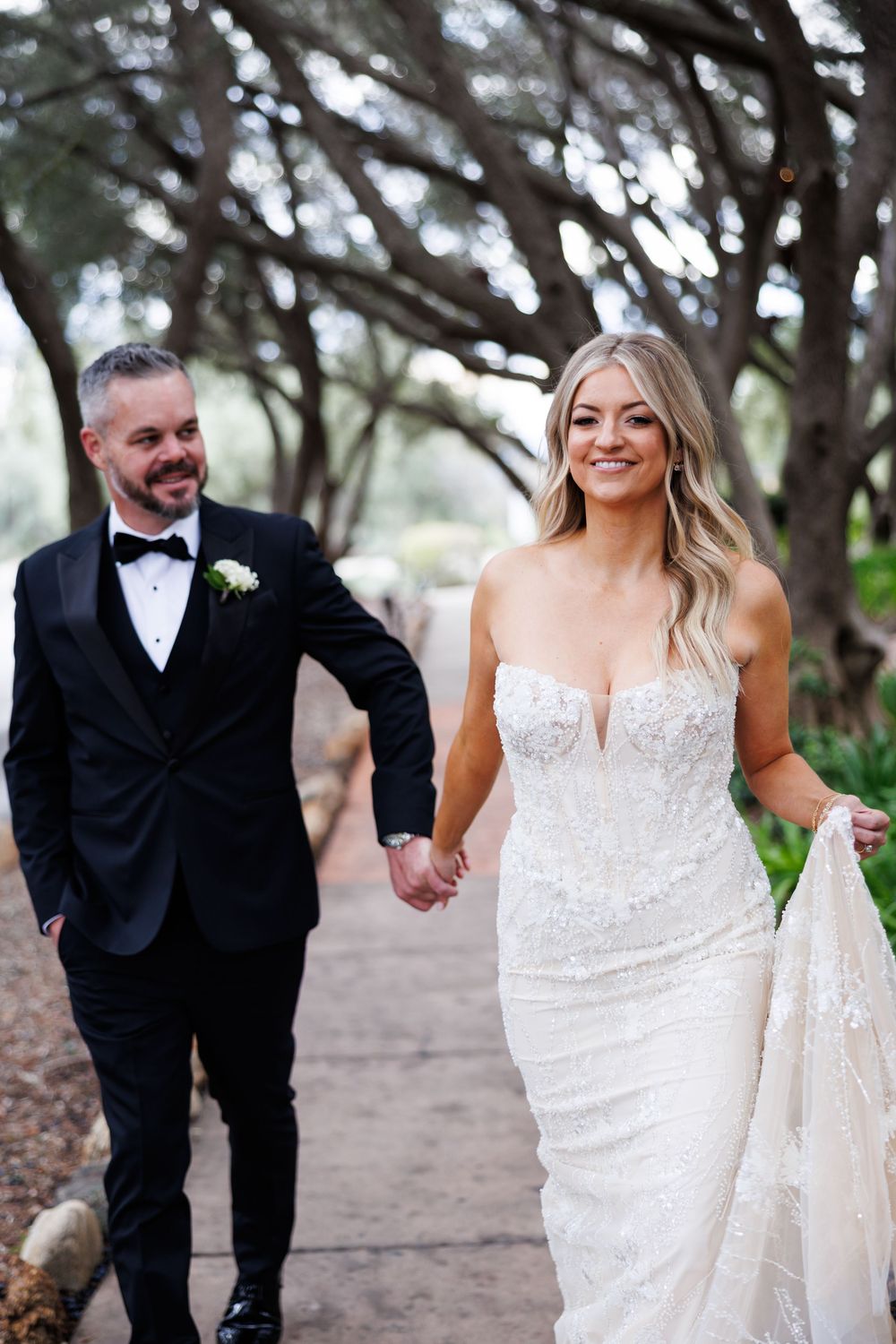 A bride and groom share playful moments while walking on a garden path.