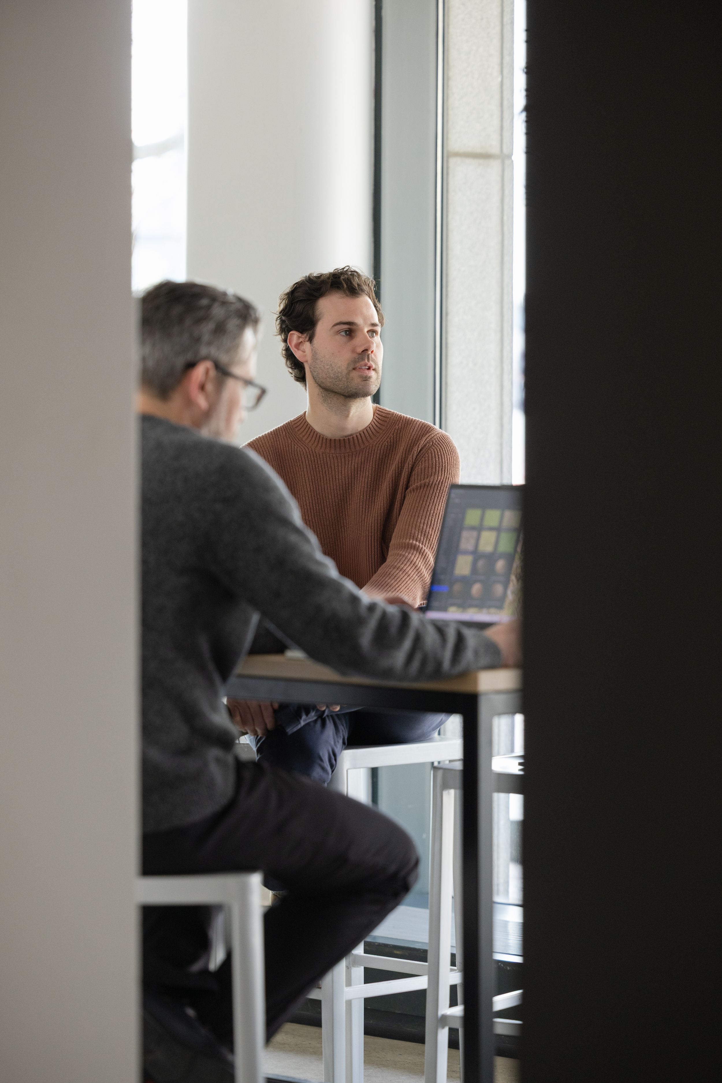 Two people sit across from each other at a table in an office having a business discussion.